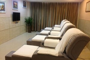 Een kamer met massagestoelen, een flatscreen televisie en een gordijn als decor.