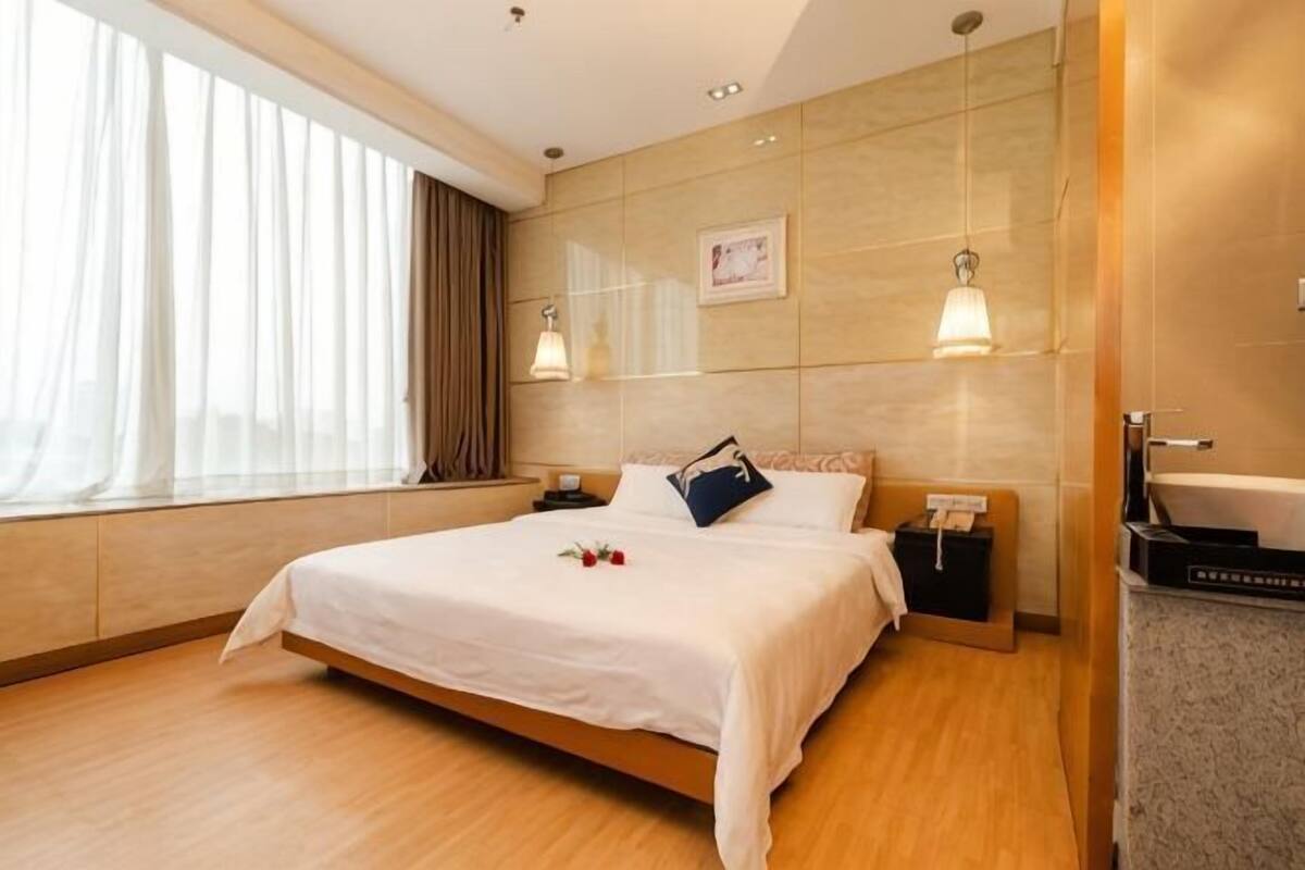 Et hotelværelse med seng, sengebord, lampe og udsigt udad.