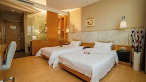 Quarto de hotel com duas camas, uma escrivaninha, uma cadeira, uma mesa de cabeceira, um vaso com flores e um quadro na parede.