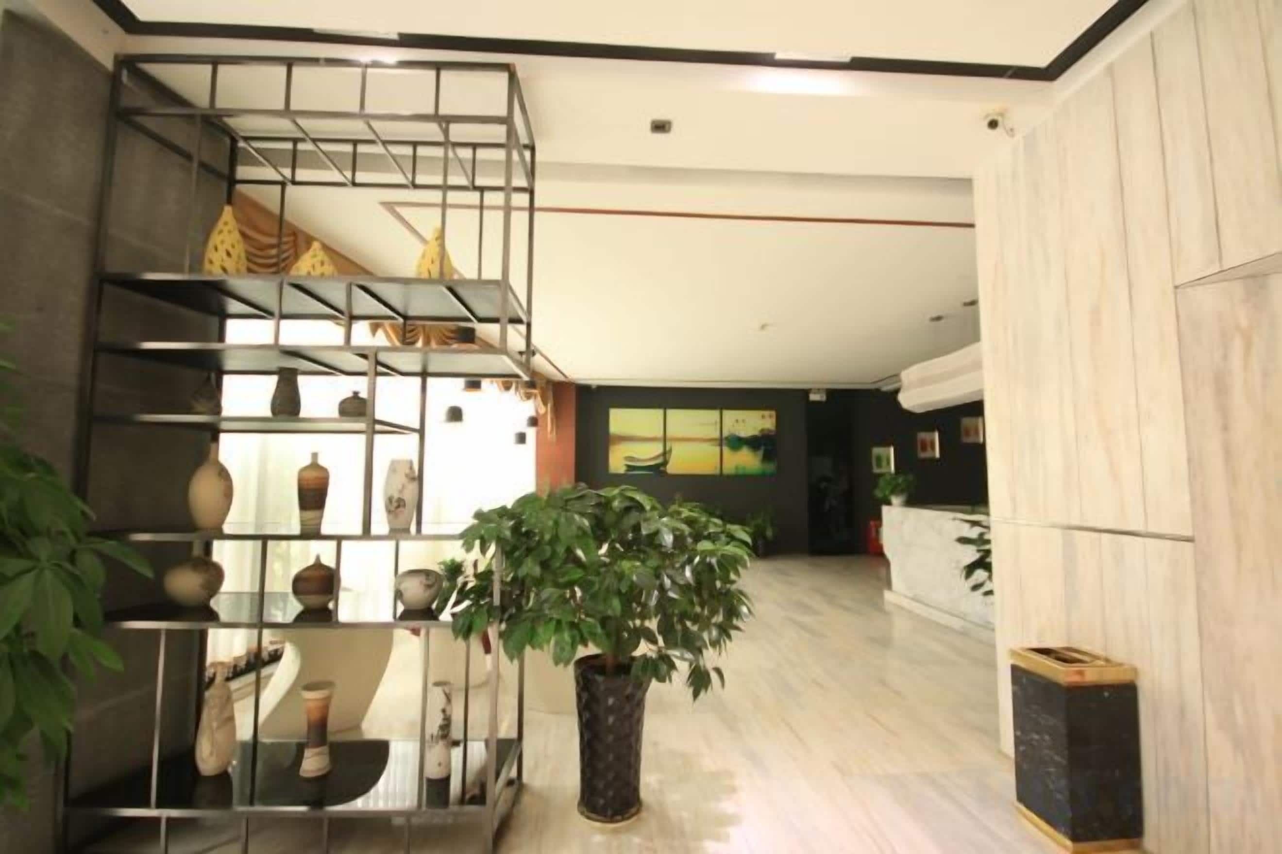 A hotel lobby with a central plant, a staircase, and a reception desk.