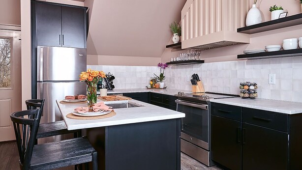 A modern kitchen with dark cabinetry, a stainless steel refrigerator, a central island with a vase of flowers, and a built-in oven. - East Nashville Guesthouse close to everything & Pet-Friendly! (Nashville)