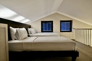Ein Schlafzimmer mit zwei Betten, einer geneigten Decke und zwei Fenstern.
