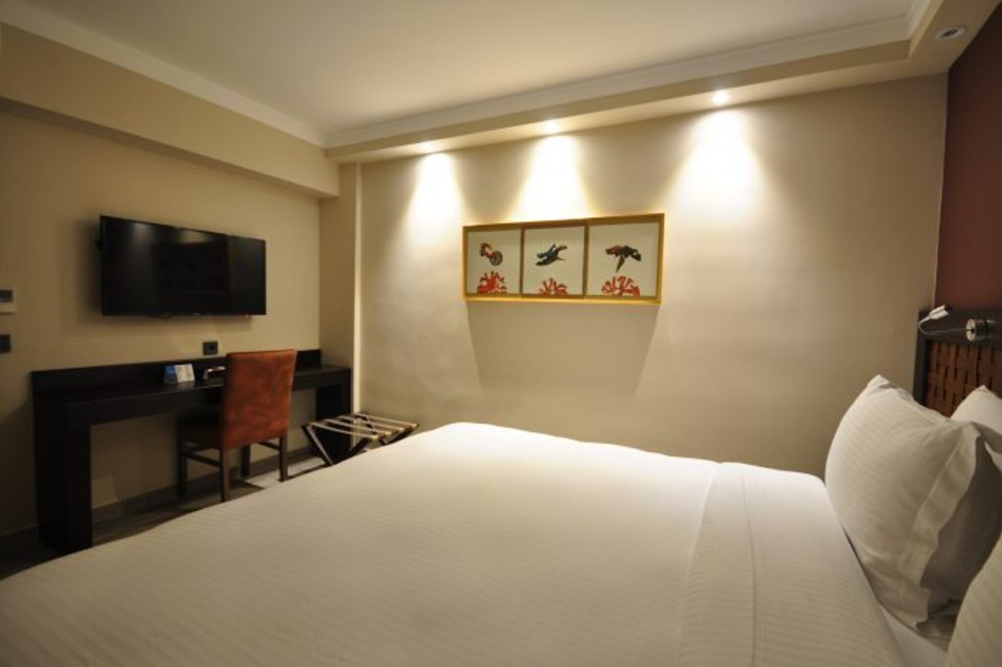 Ein Hotelzimmer mit Bett, Schreibtisch, Sessel, Flachbildfernseher und Wandbildern.