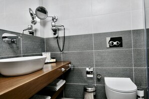 Ein modernes Badezimmer mit einem großen weißen Waschbecken, einem Spiegel, einer Duschbrause und einer Toilette.