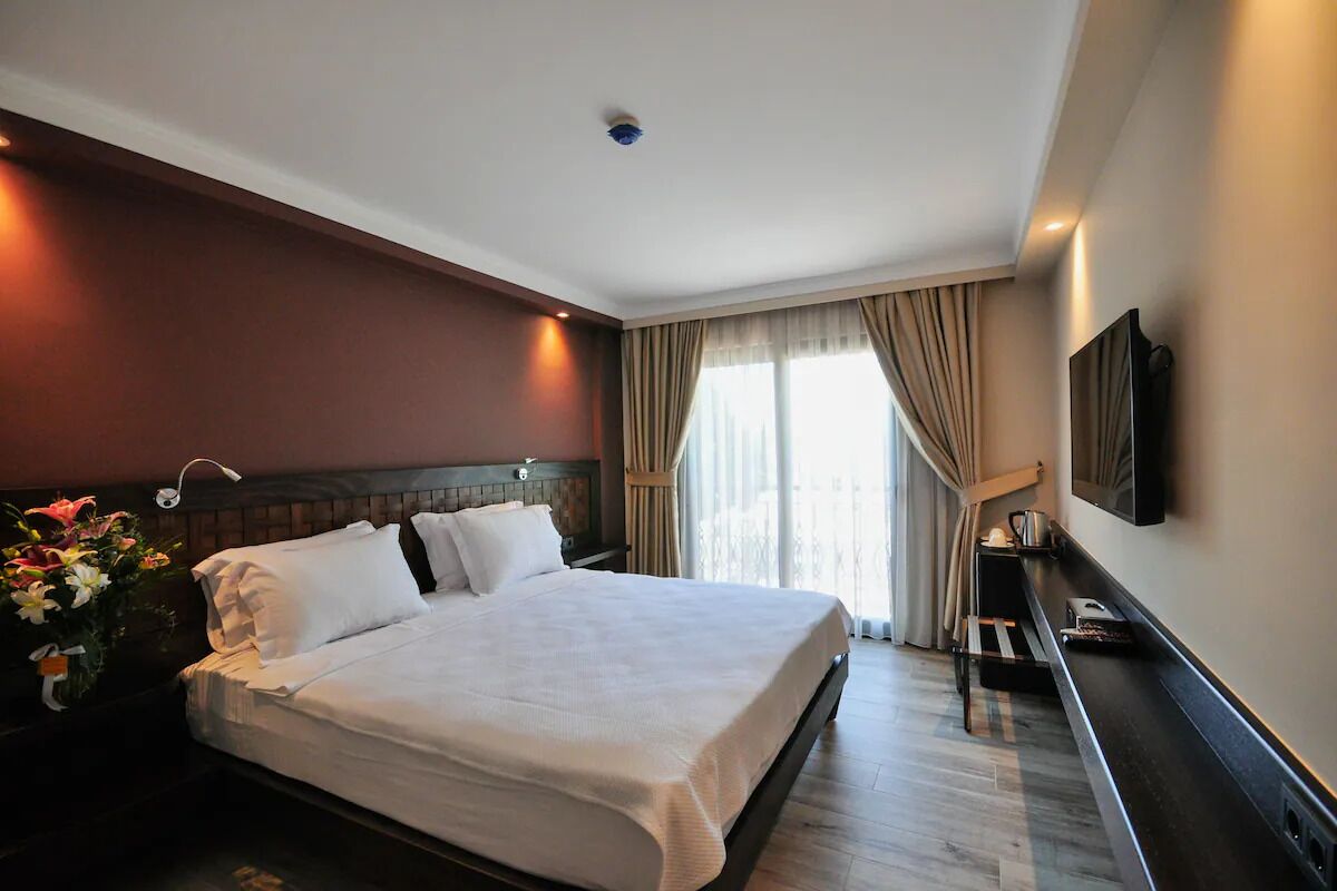 Ein modernes Hotelzimmer mit einem großen Bett, einem flachbildfernseher an der Wand und einem Nachttisch mit Lampe.