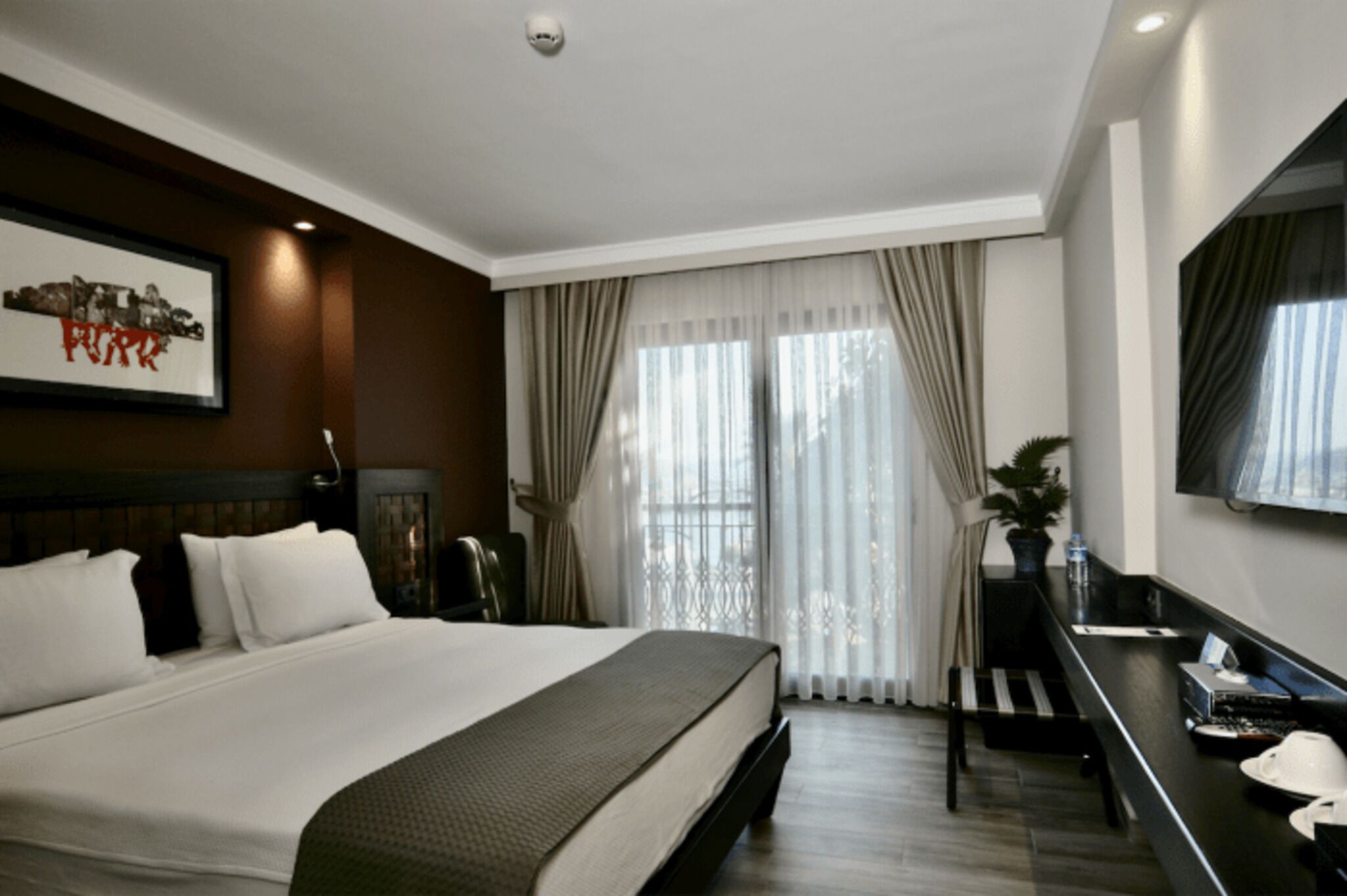 Ein Hotelzimmer mit einem großen Bett, einem Schreibtisch mit Stuhl, einem Fernseher und einem Fenster mit Vorhängen.