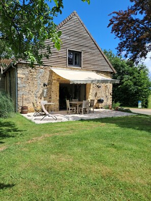 A stone house with a sloped roof, a covered patio with a table and chairs, and a stone barrel. - Old barn converted into a loft (Colombiers)