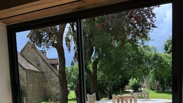 A room with a large window, a stone fireplace, and a wooden table with chairs outside.