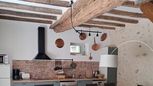 A modern kitchen with a brick backsplash, wooden beams, and a dining area with a glass table and chairs.