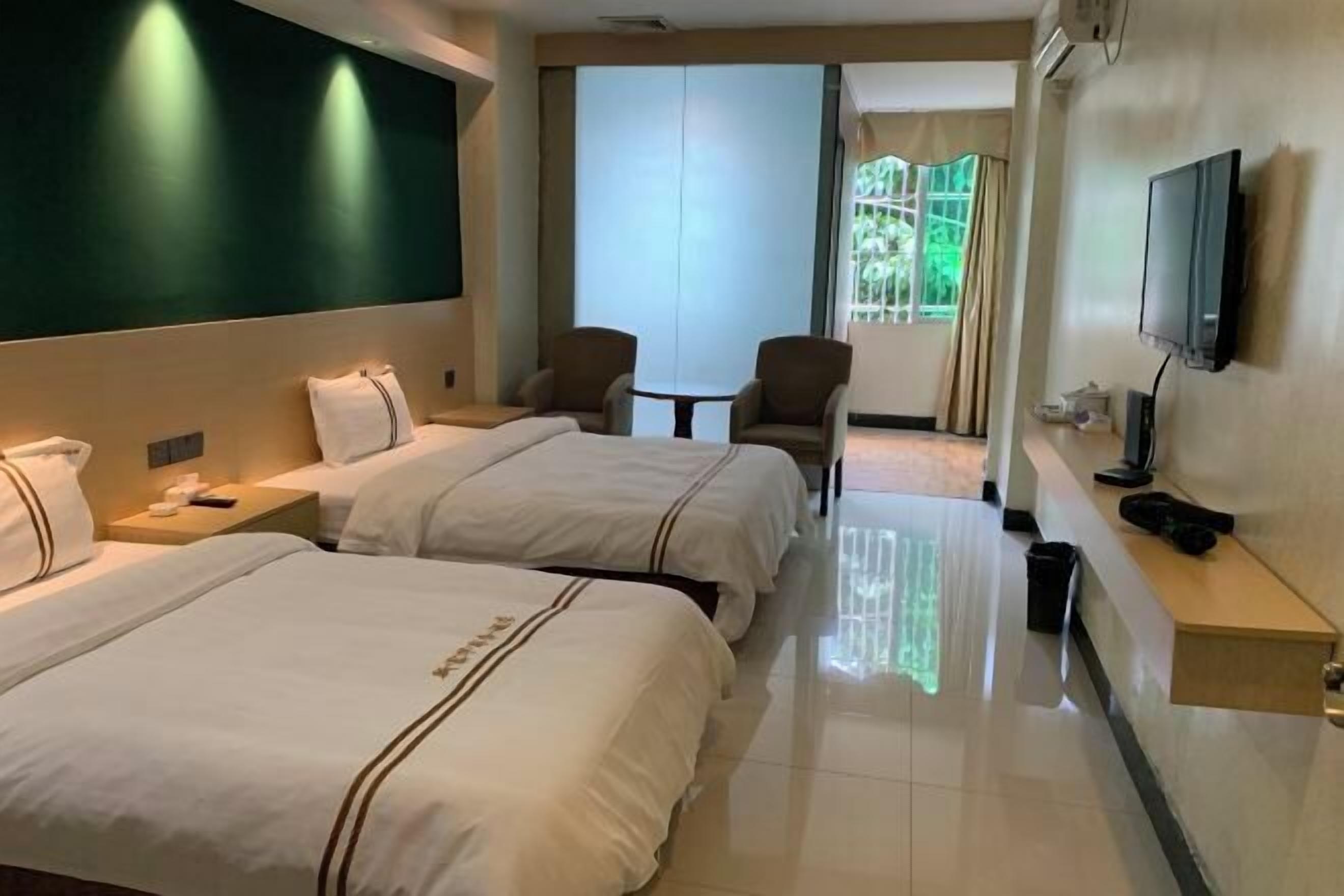 Habitación de hotel con dos camas, televisión, una mesita y ventana con cortinas.