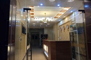 A hotel corridor with a reception desk, a chandelier, and a refrigerator.