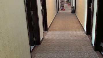A hallway with patterned carpet, doors on both sides, and a person in the distance.