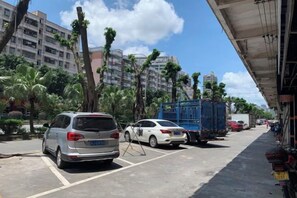 A parking area with vehicles, including a white car and a blue truck, and a building with multiple floors in the background. - Xinfuhua Business Hotel (Taishan)