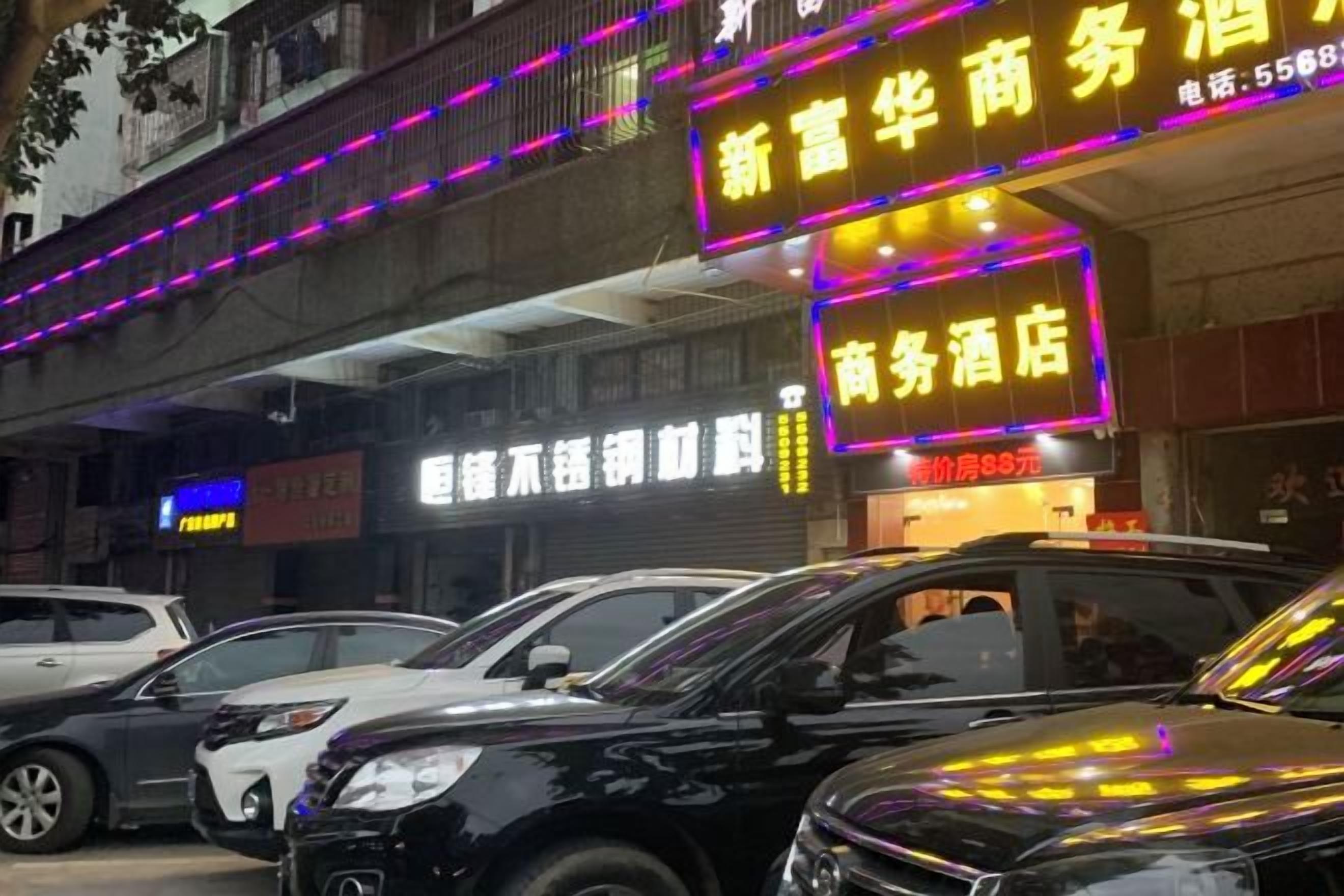 A commercial building with neon signage, parked cars, and a visible storefront.
