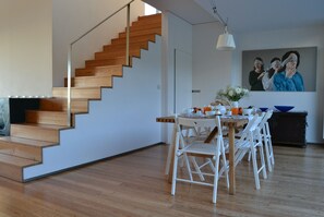 Ein modernes Interieur mit einer Holztreppe, einem Essbereich mit weißen Stühlen und einem Gemälde an der Wand.