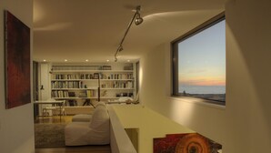 Una sala de estar moderna con una amplia estantería, un sofá blanco y vistas a la puesta de sol a través de un ventanal grande.