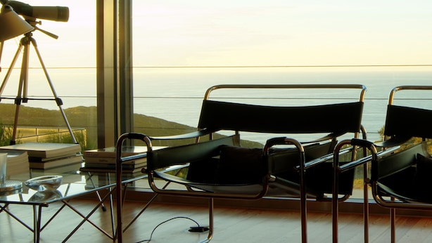Una habitación con dos sillas negras, un telescopio y vistas al océano.
