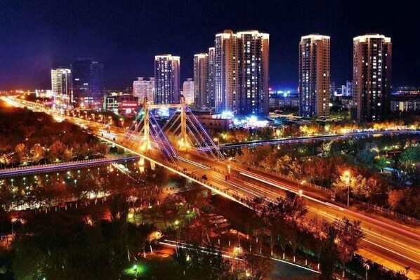 Un paisaje urbano nocturno con rascacielos iluminados, un puente y una carretera bien iluminada.