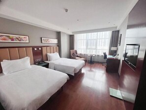 A hotel room with two beds, a desk, a chair, a TV, and large windows.