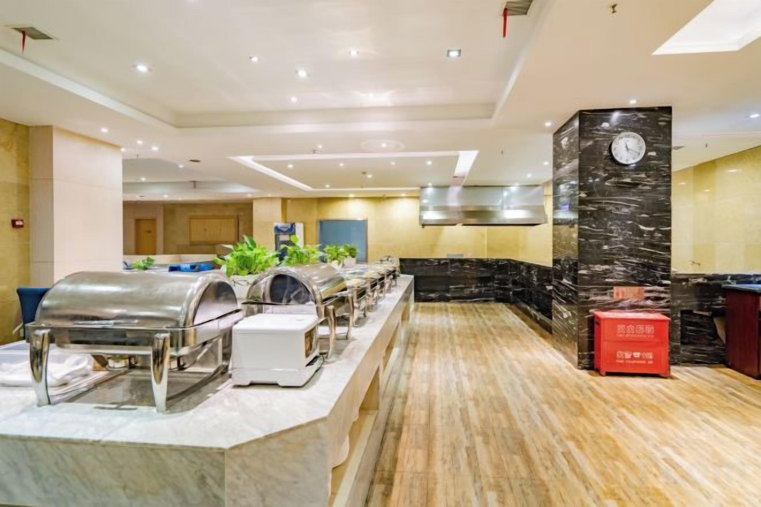 A buffet area with multiple self-service stations, a clock on a pillar, and a modern kitchen in the background.