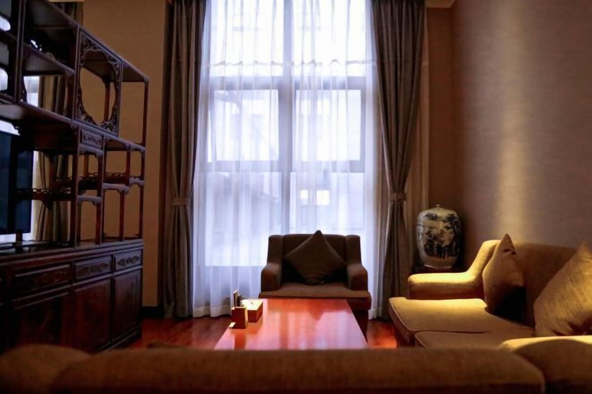 Una sala de estar con un sofá, un mueble de madera y un ventanal con cortinas.
