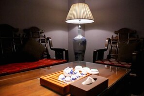Una habitación tenuemente iluminada con una mesa de madera dispuesta para tomar té, una lámpara y muebles tradicionales.