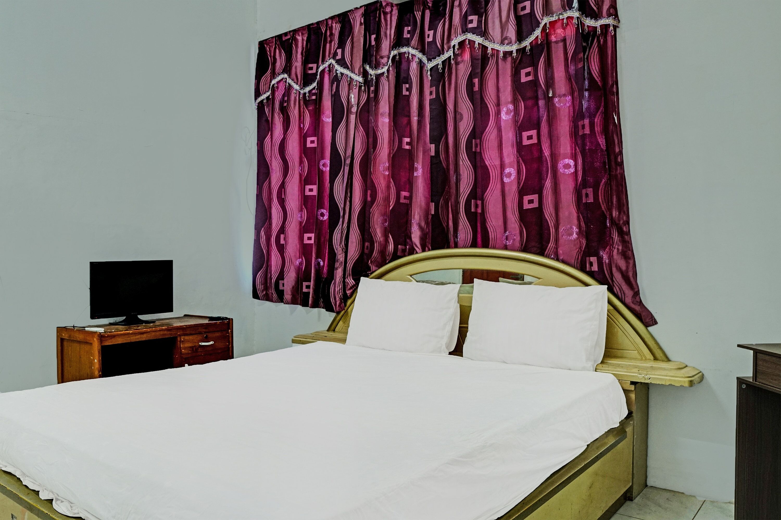 Una cama individual con ropa de cama blanca, un cabecero de madera y una mesita de noche con un televisor.