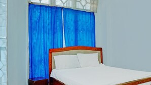 A single bed with a wooden frame and white bedding in a room with a window covered by blue curtains. - Hotel O Kost Axcel (Banjarmasin)