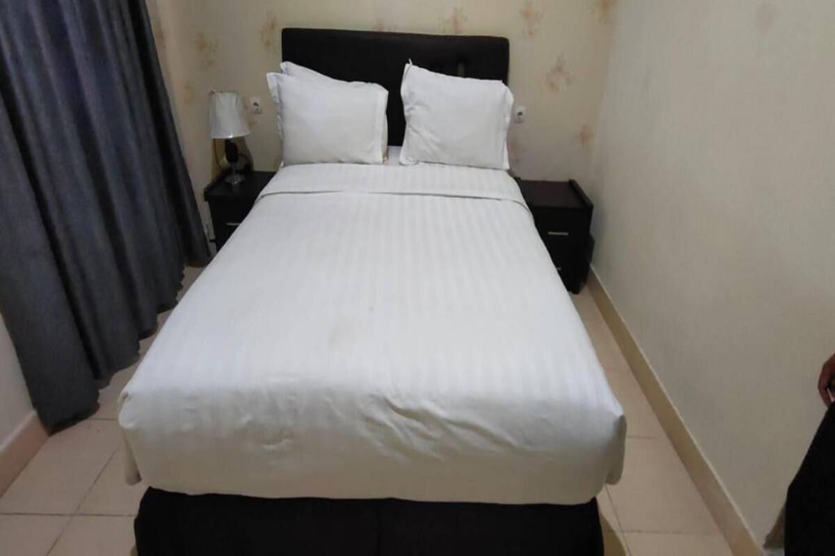 Une chambre d’hôtel standard, comprenant un lit, deux oreillers, une table de chevet avec une lampe et un rideau.