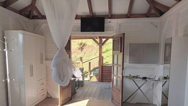 Et soveværelse med seng, garderobeskab, fjernsyn og balkon med udsigt over naturen.