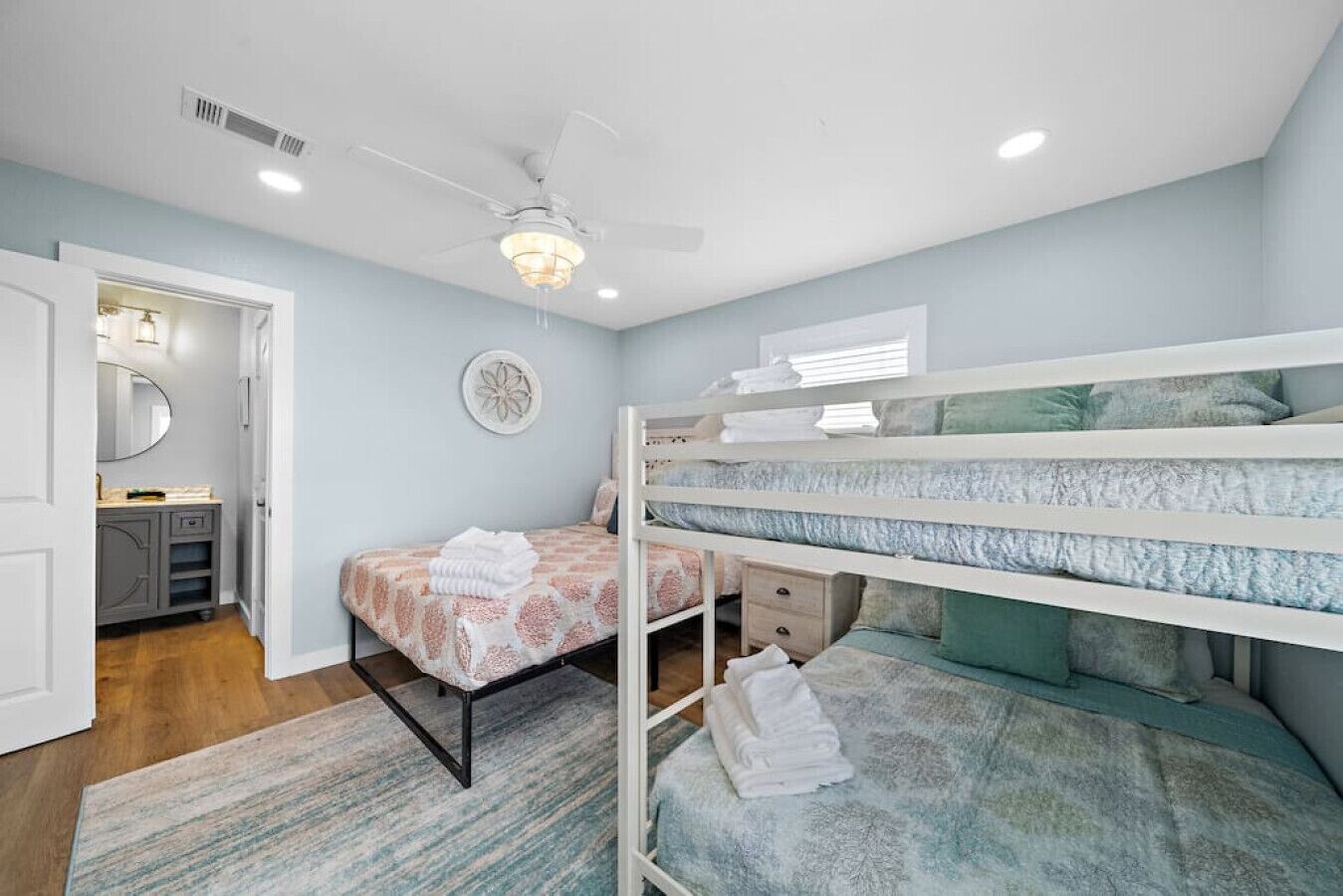 A bedroom with bunk beds, a ceiling fan, a bedside table, and a small cabinet.