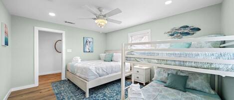 A bedroom with bunk beds, a ceiling fan, and a blue patterned rug.