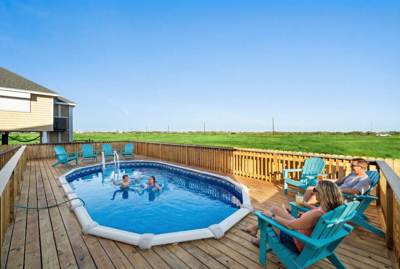 An outdoor swimming pool with a wooden deck, surrounded by chairs and a wooden fence.