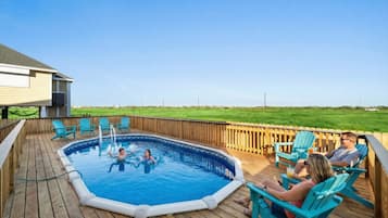 An outdoor swimming pool with a wooden deck, surrounded by chairs and a wooden fence.