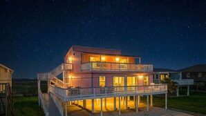 A two-story house with a balcony and a deck, surrounded by a grassy area. - Relax in Beachside Comfort with Stunning Views (Galveston)