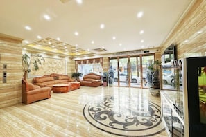 Een hotellobby met een receptiebalie, een zithoek en een grote glazen deur naar buiten.