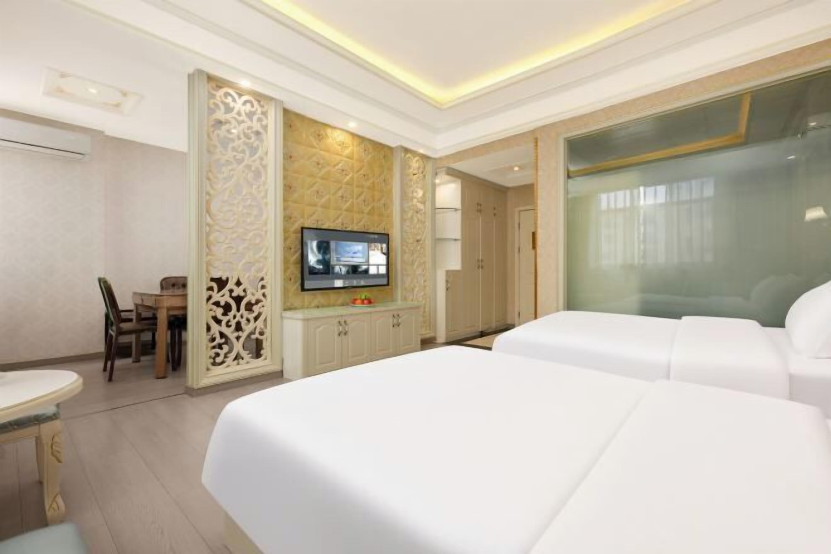 A hotel room with two beds, a TV, a desk with a chair, and a decorative wall panel.