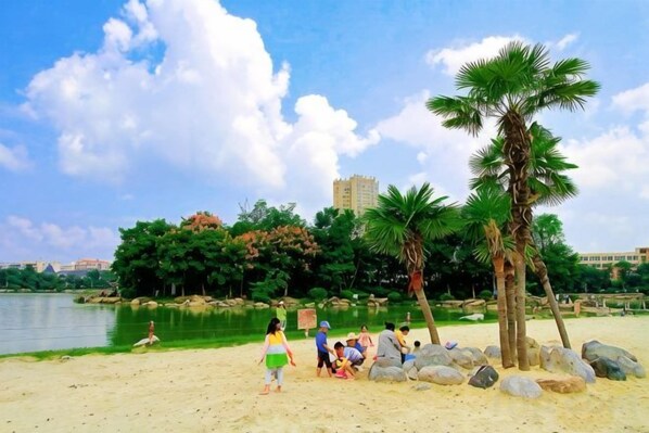 Een strand met palmbomen, een meer en een gebouw op de achtergrond.
