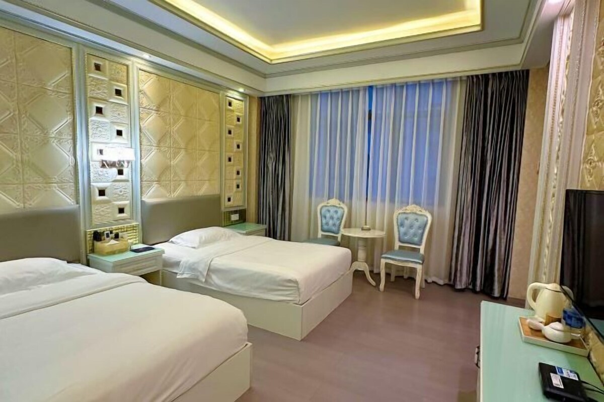 A hotel room with two beds, a small table, a chair, and a TV.