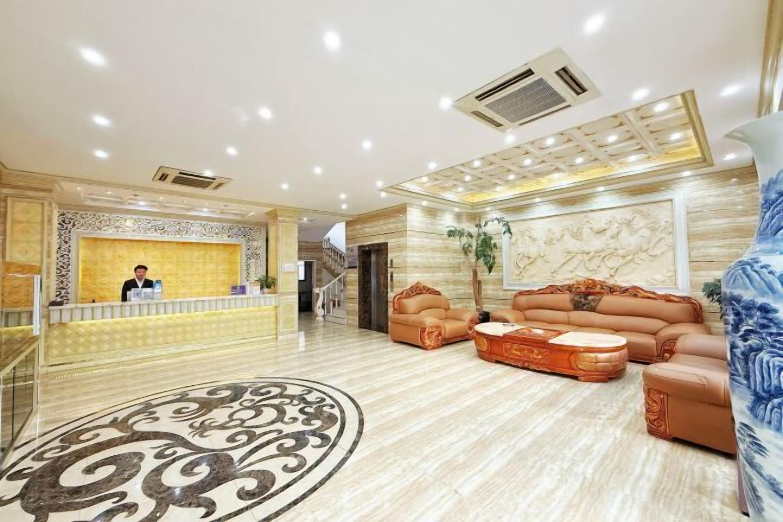 A hotel lobby with a reception desk, a sofa set, a patterned floor, and a decorative wall.