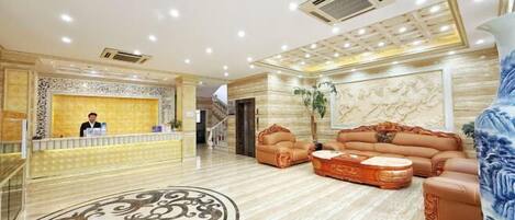 A hotel lobby with a reception desk, a sofa set, a patterned floor, and a decorative wall.