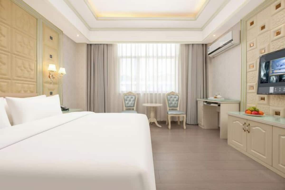 A hotel room with a bed, a desk, a TV, and a small table with chairs.