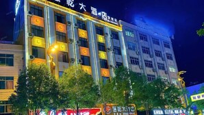 Un hôtel à plusieurs étages, doté d’une enseigne lumineuse et bordé d’une rangée d’arbres.