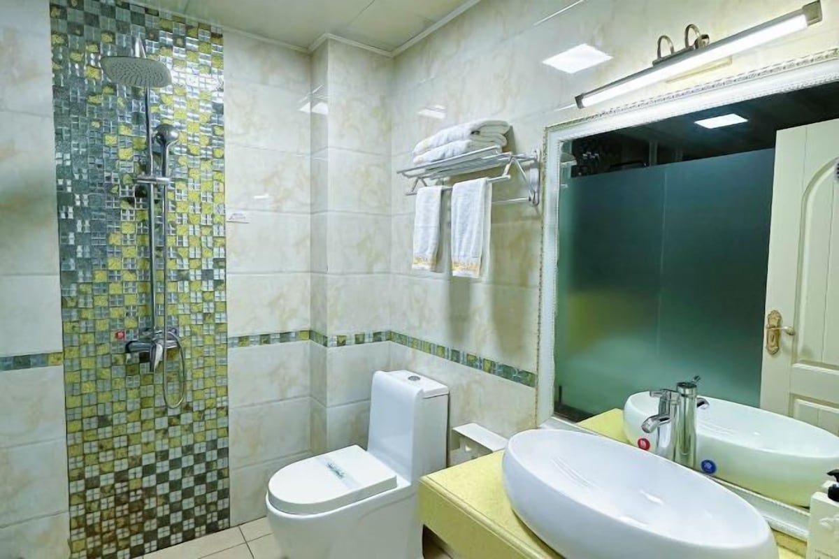 A bathroom with a shower, toilet, sink, and a large mirror.