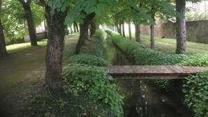 A serene garden with a narrow water channel, neatly trimmed hedges, and a wooden bridge. - VILLA DES PROMENADES, 5* atypical in a National Forest Park, European Ecolabel (Vanvey)
