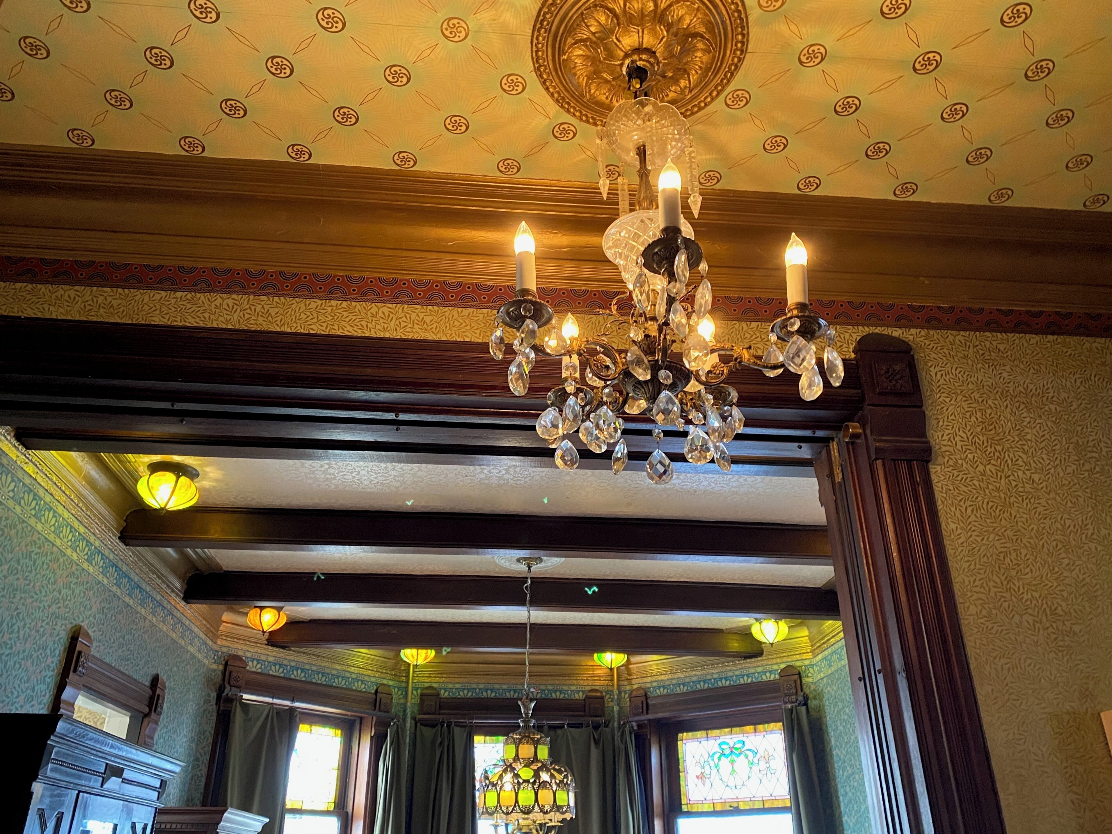 A grand chandelier with multiple candles, ornate ceiling patterns, and a large stained glass window.