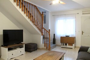 A living room with a wooden staircase, a flat-screen TV, a sofa, a coffee table, and a door with a curtain. - 3 Bed 2 Bath Next to Communal Pool, Golf, beaches and Villamartin Plaza (Orihuela Costa)