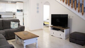 Ett modernt vardagsrum med en soffa, ett soffbord och en tv som står på ett tv-bord. En trappa med träspjälor leder upp till nästa våningsplan.