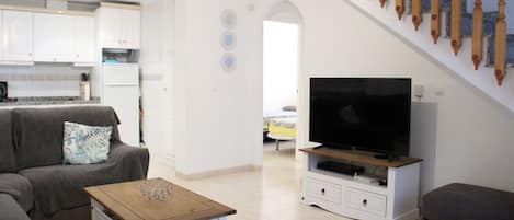 A modern living room with a sofa, a coffee table, and a TV on a stand. There is a staircase with wooden balusters leading to another level.