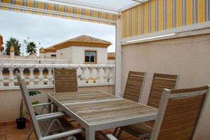 An outdoor patio with a table and chairs, a potted plant, and a view of a building with a tiled roof. - 3 Bed 2 Bath Next to Communal Pool, Golf, beaches and Villamartin Plaza (Orihuela Costa)